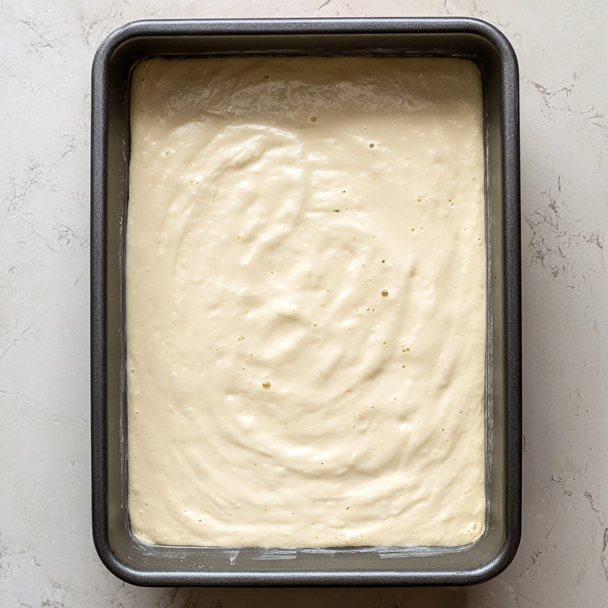 Easy Mango Tres Leches Recipe | Tropical Summer Dessert 11 Tres leches cake soaking in a creamy milk mixture inside a rectangular baking pan, photographed from above.