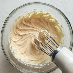 Easy Mango Tres Leches Recipe | Tropical Summer Dessert 16 Cake batter being mixed with an electric hand mixer in a glass bowl, showing a smooth and airy texture.