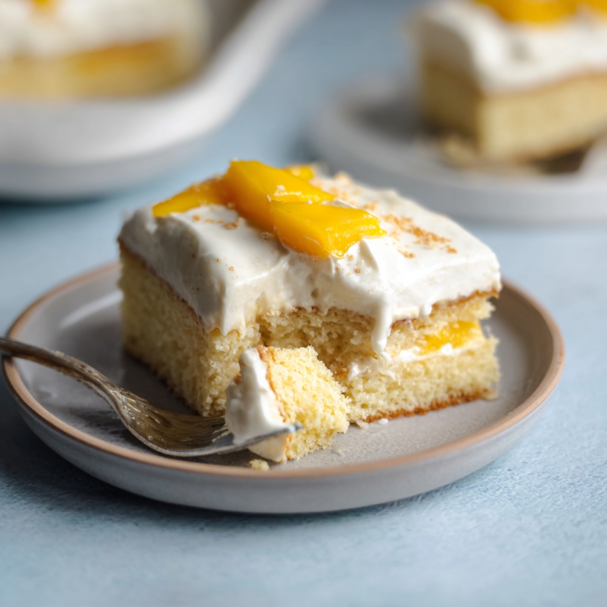 Easy Mango Tres Leches Recipe | Tropical Summer Dessert 14 Mango tres leches cake slice on a plate with a fork and a bite removed, showing moist sponge and creamy layers.