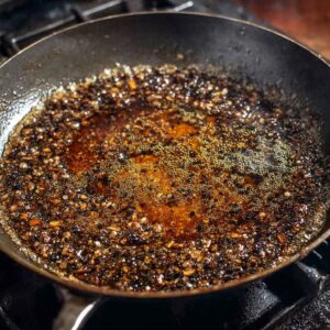 Easy Peppercorn Sauce Recipe | Ready in 20 Minutes 16 A close-up of the peppercorn sauce in a skillet, reducing and darkening as it thickens, with the spoon making marks in the smooth, glossy sauce.