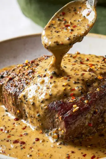 Easy Peppercorn Sauce Recipe | Ready in 20 Minutes 3 peppercorn sauce recipe A spoon drizzling the rich, peppercorn sauce over a juicy steak, creating a glossy layer of sauce that enhances the flavors of the meat.