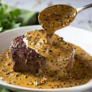 Easy Peppercorn Sauce Recipe | Ready in 20 Minutes 20 A close-up of creamy peppercorn sauce being spooned generously over a perfectly cooked steak, with visible peppercorns and a glossy texture.