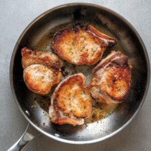 Easy Pineapple Pork Chops Recipe | Ready in 20 Minutes 16 Pork chops browning in a stainless steel skillet, showing a golden crust during the cooking process.