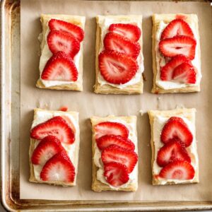 Best Strawberry Danishes | 5 Ingredients & Flaky 17 “Puff pastry squares on a baking tray topped with cream cheese filling and fresh sliced strawberries before baking.”