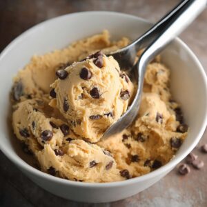 Easy Brookies Cookies Recipe | Half Cookie, Half Brownie 15 Vanilla chocolate chip cookie dough in a white bowl with a metal scoop lifting a portion of dough.