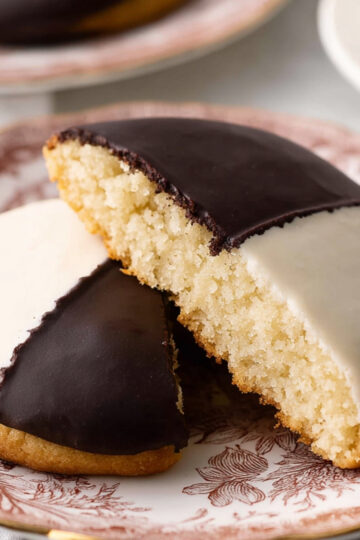 Black and White Cookies | Easy Homemade Recipe Guide 1 Black and White Cookies sliced open on a patterned plate, half covered in chocolate icing and half in vanilla icing.
