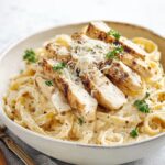 Chicken Alfredo pasta topped with sliced chicken and Parmesan cheese