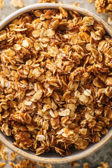 Easy Granola Recipe: Crunchy Clusters in Just 30 Minutes 14 Granola Recipe Top-down shot of homemade granola in a ceramic bowl with oat clusters scattered around, golden brown color, crunchy texture, rustic background, soft natural lighting, editorial food photography