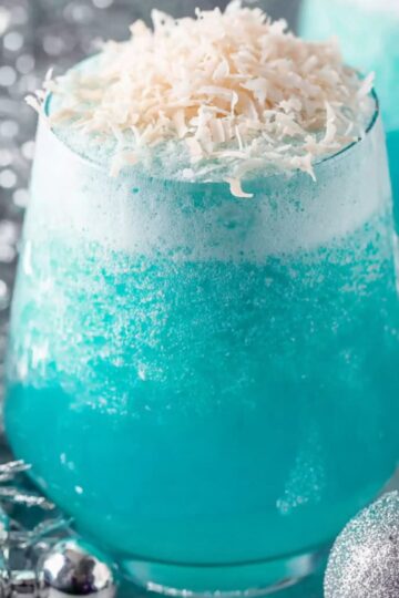 Jack Frost Cocktail Recipe | 5-Minute Frozen Drink 1 Jack Frost Cocktail A close-up shot of a festive blue cocktail topped with shredded coconut, surrounded by silver holiday decorations such as ornaments and tinsel."