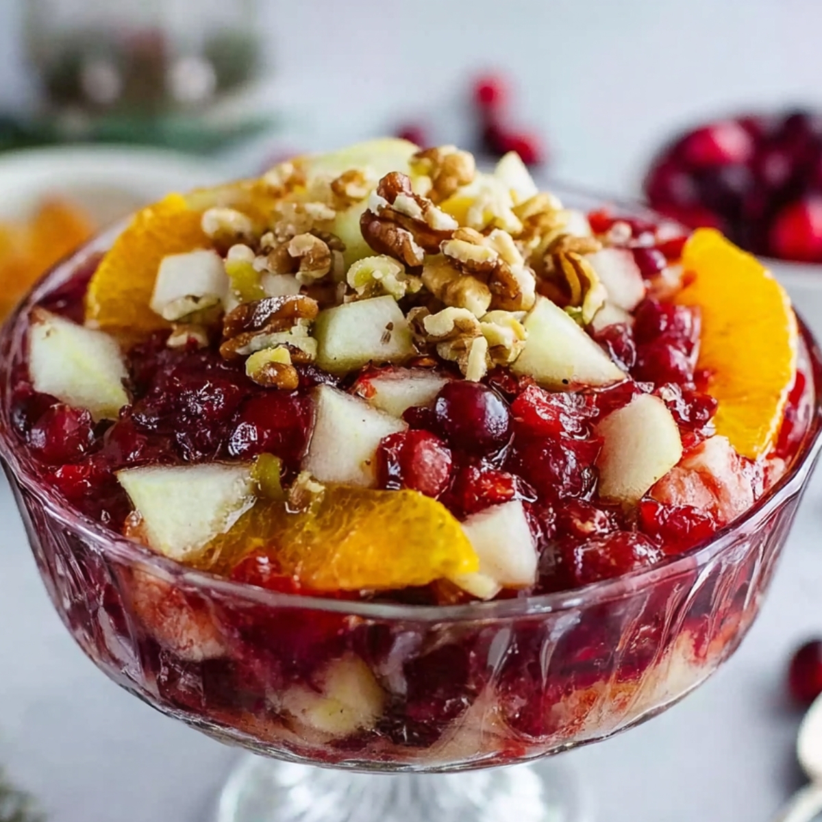 Jello Fruit Salad A beautifully presented fruit salad with cranberries, topped with orange slices, pear pieces, and chopped nuts in a clear glass bowl, perfect for a festive occasion.
