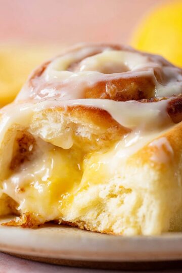 Lemon Cinnamon Rolls Recipe | Soft, Tangy & Easy 8 Lemon Cinnamon Rolls Close-up food photography of a soft lemon sweet roll cut open, filled with gooey lemon sugar filling and topped with glossy lemon cream cheese frosting, bright warm lighting, shallow depth of field, bakery-style dessert, ultra realistic, high detail, soft pastel background