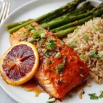Orange Glazed Salmon served with roasted asparagus and brown rice, garnished with fresh herbs and a blood orange slice.