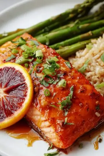 Orange Glazed Salmon Recipe | Ready in 25 Minutes 1 Orange Glazed Salmon served with roasted asparagus and brown rice, garnished with fresh herbs and a blood orange slice.