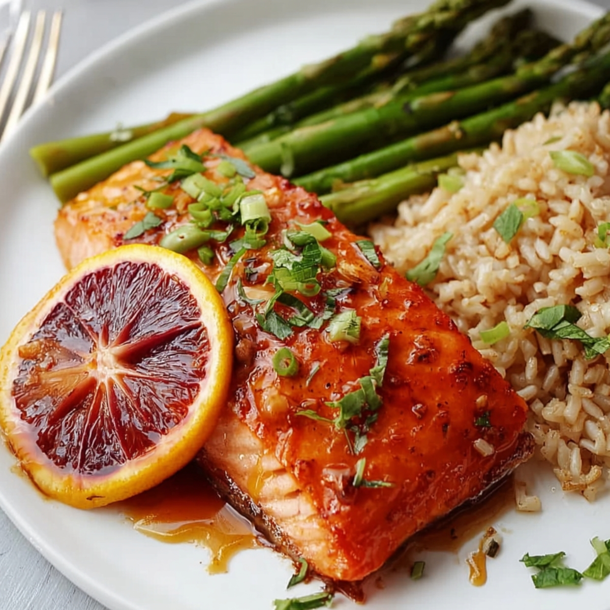 Orange Glazed Salmon served with roasted asparagus and brown rice, garnished with fresh herbs and a blood orange slice.