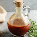 Red Wine Vinaigrette Homemade red wine vinaigrette stored in a small glass bottle with a cork stopper, set on a stone surface with fresh thyme.