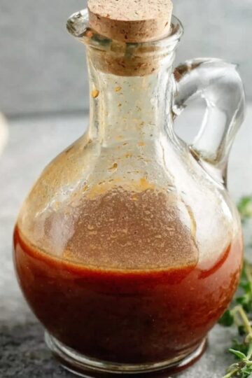 Best Red Wine Vinaigrette Recipe (Homemade in Minutes) 4 Red Wine Vinaigrette Homemade red wine vinaigrette stored in a small glass bottle with a cork stopper, set on a stone surface with fresh thyme.