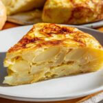 Spanish tortilla Close-up of a slice of Spanish tortilla on a white plate with bread, layered potatoes visible inside, golden crust, warm natural light, Mediterranean dish photography