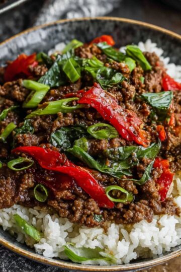 Thai Basil Beef Recipe - Quick, Easy & Ready in 25 Min 9 Thai Basil Beef A bowl of Thai basil beef served on rice, garnished with green onions and fresh basil leaves."
