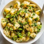 Turkish potato salad Overhead view of Turkish potato salad in a white bowl, featuring tender potatoes mixed with green onions, parsley, spices, and olive oil on a marble background.