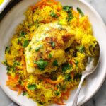 Turmeric Chicken and Rice Casserole A plate of turmeric chicken and rice, showcasing a golden-brown chicken breast resting on a vibrant bed of yellow rice, topped with freshly chopped cilantro and shredded carrots. The rice looks fragrant and full of flavor, creating a colorful and appetizing dish.