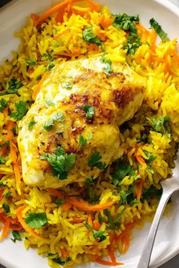 Healthy Turmeric Chicken and Rice Casserole 9 Turmeric Chicken and Rice Casserole A plate of turmeric chicken and rice, showcasing a golden-brown chicken breast resting on a vibrant bed of yellow rice, topped with freshly chopped cilantro and shredded carrots. The rice looks fragrant and full of flavor, creating a colorful and appetizing dish.