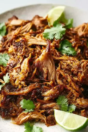 Carnitas Crockpot Recipe | 10 Ingredients, 8 Hours 1 carnitas crockpot Close-up food photography of crispy Mexican carnitas, golden-brown shredded pork piled on a white ceramic plate, garnished with fresh cilantro and lime wedges, juicy texture, crispy edges, natural daylight, high detail, shallow depth of field, food magazine style
