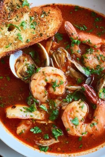Easy Cioppino Recipe | Restaurant-Quality Seafood Stew 8 cioppino recipe A beautiful bowl of cioppino seafood stew filled with shrimp, clams, and fish, swimming in a rich, flavorful tomato broth. Fresh parsley and a side of crispy garlic bread add the perfect finishing touch
