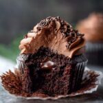 cream-filled chocolate cupcakes with a bite taken out, revealing a gooey chocolate ganache center and topped with chocolate frosting and chocolate sprinkles, moist crumb, cupcake wrapper peeled back.
