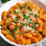 Creamy tomato gnocchi served in a dish, topped with grated Parmesan cheese and fresh parsley.