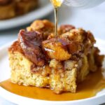 crockpot french toast A serving of slow-cooked French toast casserole, drizzled with syrup on a white plate. The French toast is golden-brown with cinnamon and caramelized sugar on top, showing a close-up shot of the rich texture and sweetness.