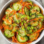 cucumber and carrot salad Fresh cucumber and carrot salad with sliced green onions and sesame seeds, served in a white bowl, showcasing vibrant colors and textures, perfect for a healthy and refreshing dish.