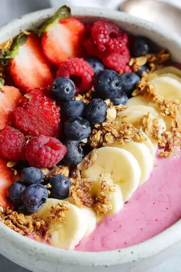 Healthy Raspberry Smoothie Bowl Recipe 14 raspberry smoothie bowl Raspberry smoothie bowl topped with granola, fresh berries, and banana slices, placed on a marble countertop.