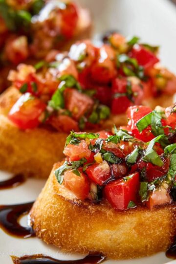 Easy Tomato Bruschetta Recipe | Ready in 37 Minutes 3 tomato bruschetta on toasted bread topped with fresh tomatoes, basil, and balsamic glaze on a white plate