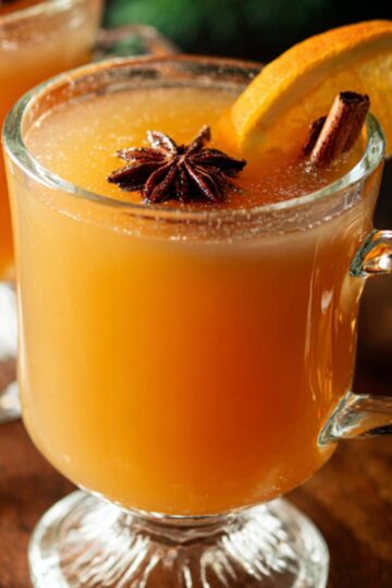 Easy 6-Ingredient Wassail Recipe | Holiday Spiced Cider 3 wassail recipe Two clear glass mugs filled with hot wassail, garnished with orange slices, cinnamon sticks, and star anise on a wooden surface.