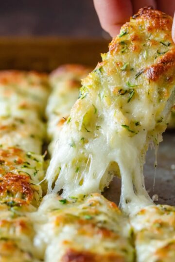 Zucchini Breadsticks Recipe | 5 Ingredients & Ready in 40 Min 21 zucchini breadsticks Hand lifting a cheesy zucchini breadstick from a baking tray with melted mozzarella stretching