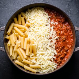 Best Baked Ziti Recipe | Feed a Crowd in Under 1 Hour 16 Overhead cooking process showing cooked ziti pasta, shredded mozzarella cheese, and tomato meat sauce arranged side by side in a pot