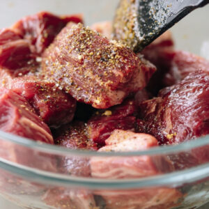 Easy Beef Mechado Recipe - Tender Filipino Tomato Beef Stew 15 Raw beef chunks seasoned with spices in a glass bowl, being mixed before cooking beef mechado.