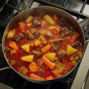 Easy Beef Mechado Recipe - Tender Filipino Tomato Beef Stew 18 Overhead view of beef mechado simmering in a pot with beef, potatoes, carrots, celery, and bell peppers in a tomato-based broth.