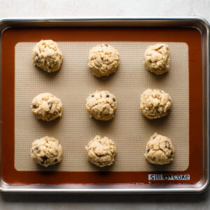 Black and White Cookies | Easy Homemade Recipe Guide 16 Raw cookie dough balls evenly spaced on a baking sheet lined with a silicone baking mat, ready for baking.