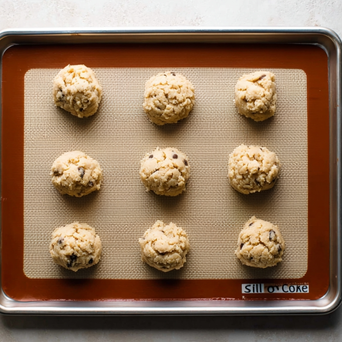 Black and White Cookies | Easy Homemade Recipe Guide 11 Raw cookie dough balls evenly spaced on a baking sheet lined with a silicone baking mat, ready for baking.