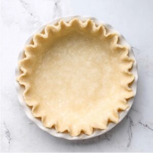 Buttermilk Chess Pie Recipe | 8 Simple Ingredients 14 Unbaked pie crust with crimped edges in a white ceramic pie dish on a marble surface.