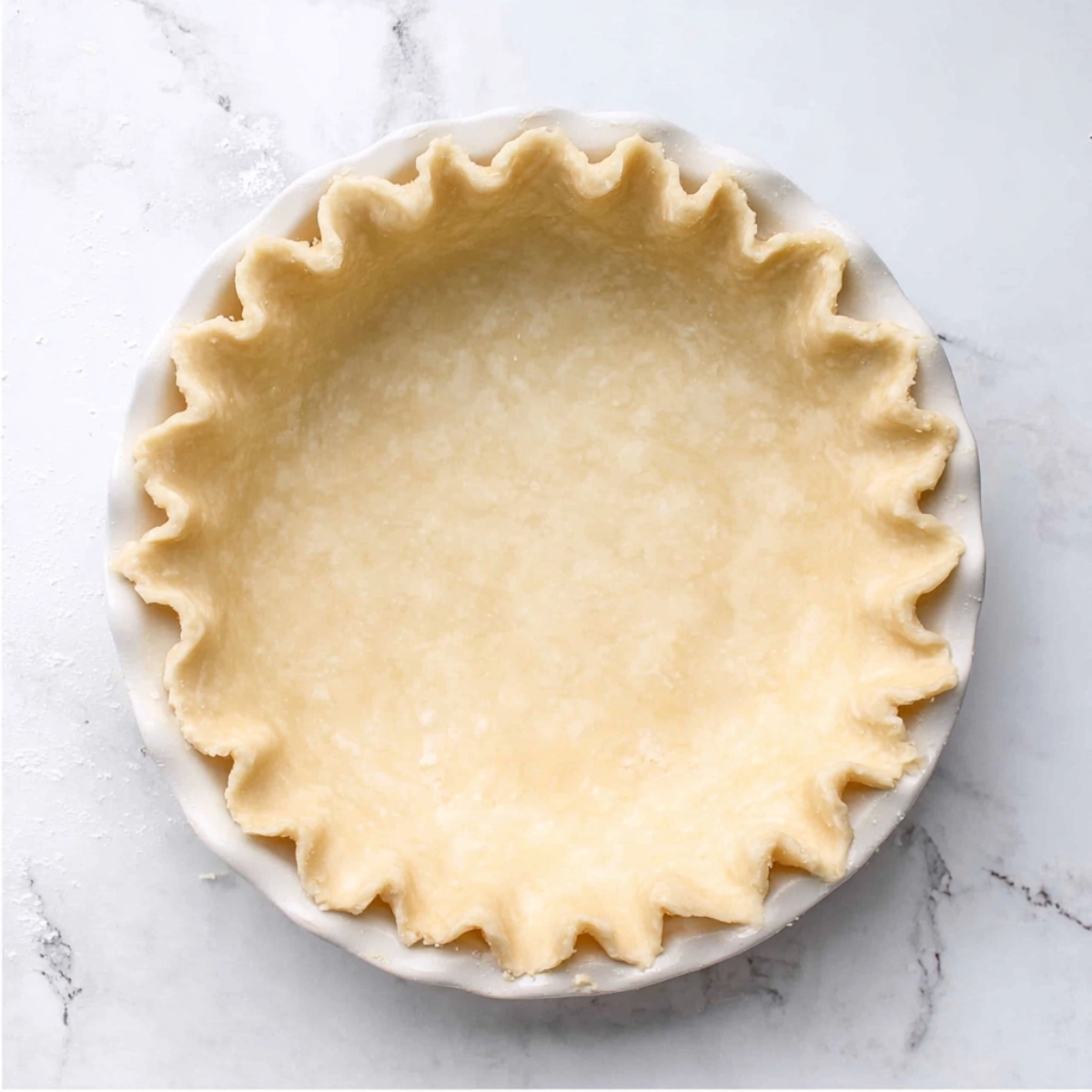 Buttermilk Chess Pie Recipe | 8 Simple Ingredients 10 Unbaked pie crust with crimped edges in a white ceramic pie dish on a marble surface.