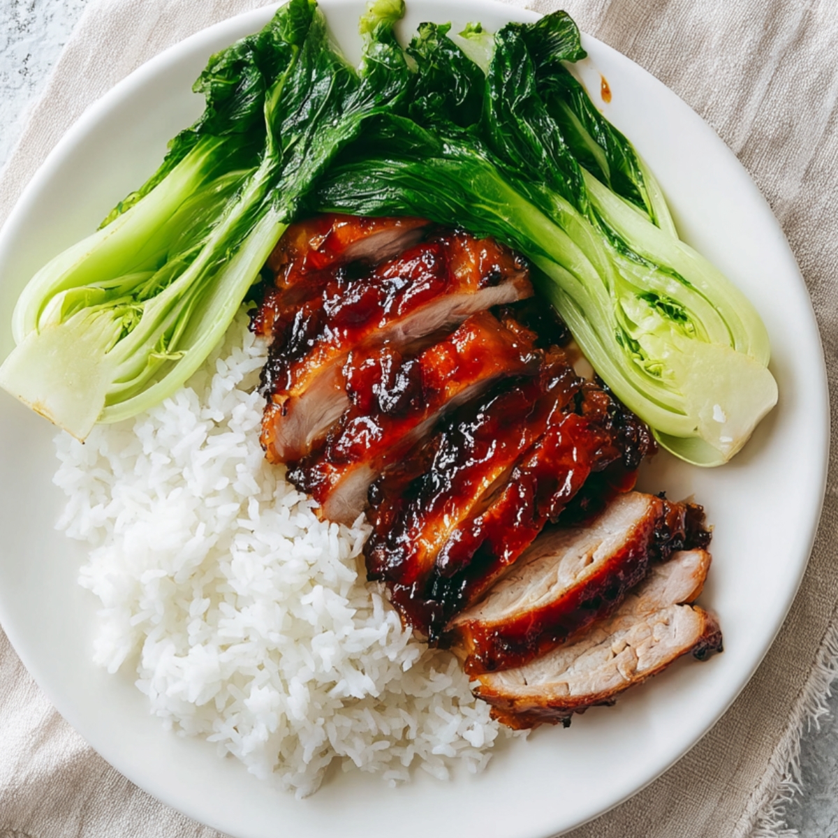 Easy Char Siu Chicken Recipe | Sticky Chinese BBQ Chicken 13 Glazed char siu chicken thigh served with steamed white rice and sautéed bok choy on a white plate, coated in sticky red barbecue sauce.