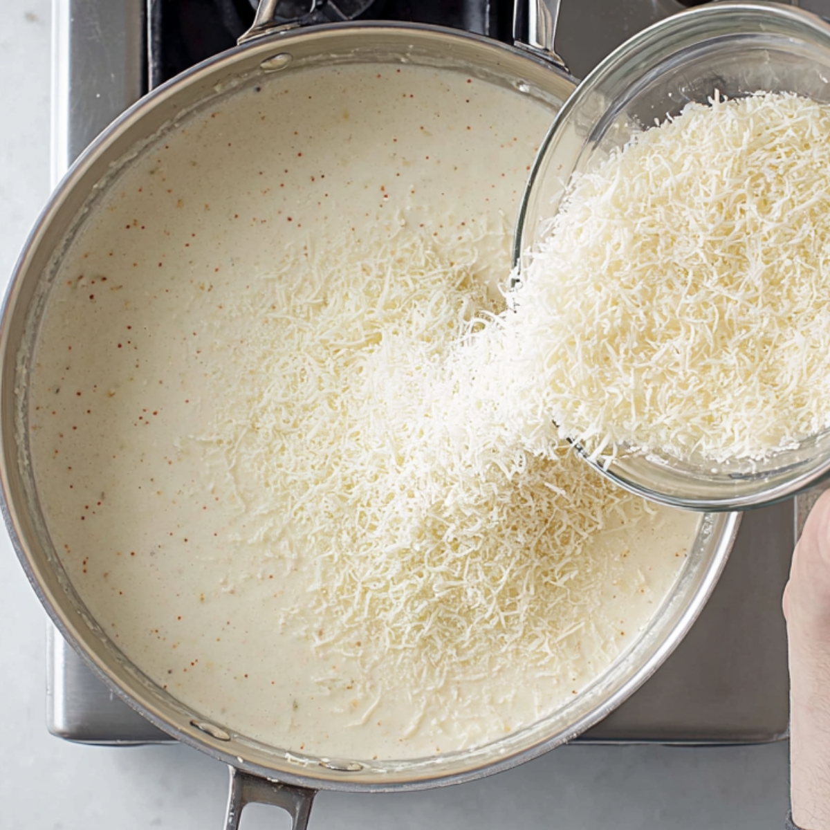 One-Pan Chicken Alfredo Recipe | Ready in 40 Minutes 11 Grated Parmesan cheese being added to a creamy Alfredo sauce in a pan