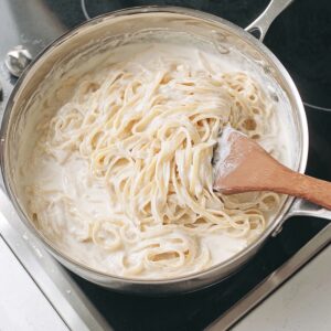 One-Pan Chicken Alfredo Recipe | Ready in 40 Minutes 18 Creamy fettuccine Alfredo pasta being stirred in a pan on the stovetop
