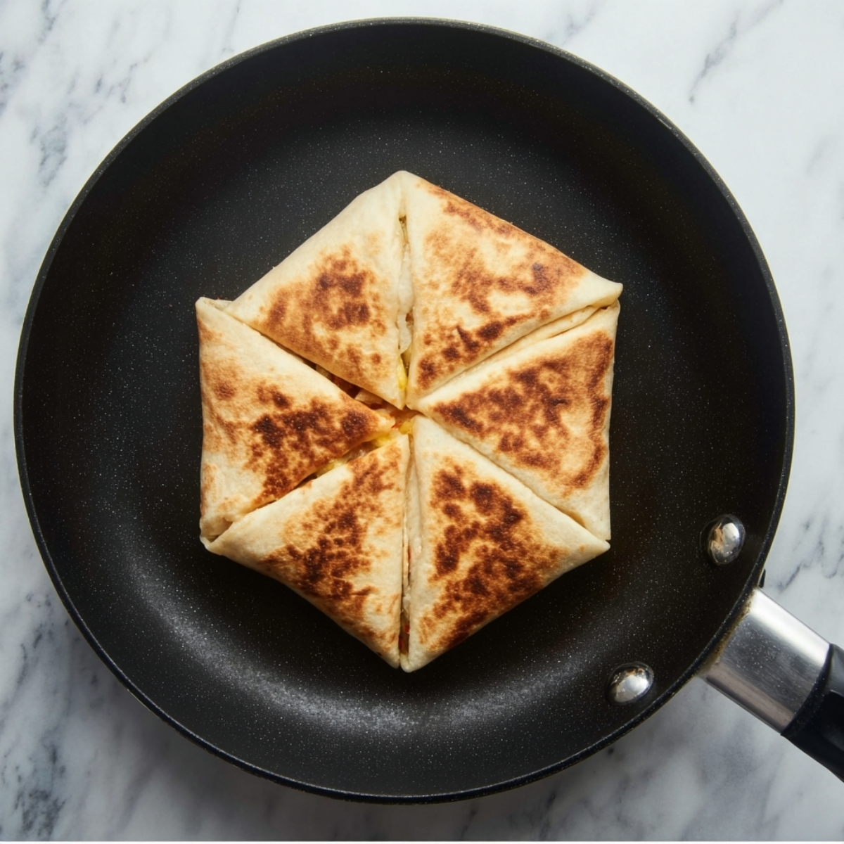 Chicken Crunch Wrap Recipe - Crispy & Ready in 30 Min 12 Top-down food photography of a folded tortilla wrap being pan-fried in a black nonstick skillet, golden brown crispy surface with triangular folds, minimal styling, marble countertop background, natural soft lighting, clean cooking process, high realism