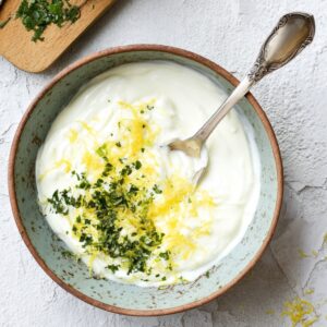 Christmas Salmon Recipe | Ready in 40 Minutes 17 “Top-down food prep shot of a ceramic bowl filled with yogurt mixed with lemon zest and fresh herbs, spoon inside the bowl, lemon and microplane grater on wooden board nearby, minimal clean styling, white textured background, bright natural light, recipe step photography.”