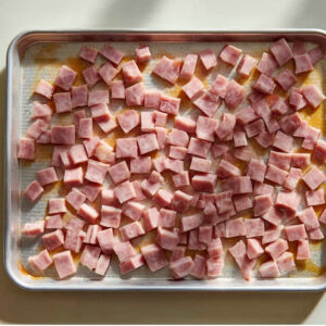Overnight Eggs Benedict Casserole Recipe | Feeds 12 16 Diced ham pieces spread evenly on a metal baking sheet, photographed from a top-down view in natural light.