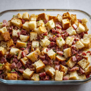 Overnight Eggs Benedict Casserole Recipe | Feeds 12 19 Glass baking dish filled with cubed bread and diced ham, evenly layered and ready for baking, photographed from above.