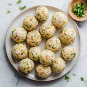 Delicious Fried Rice Balls Recipe In 3 Steps 17 Raw rice balls made from seasoned rice and vegetables arranged on a plate, visible rice grains and herbs, pre-breading stage, top-down composition, natural daylight, clean marble surface, realistic food photography